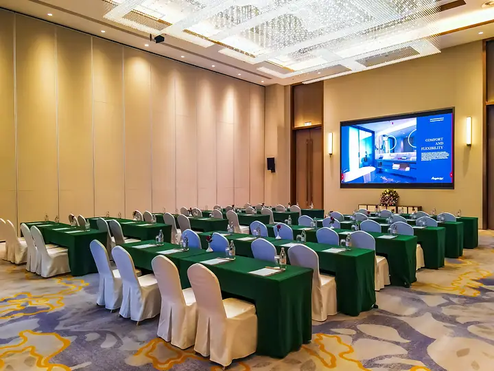 Conference hall set classroom-style: rows of tables with green cloths and white chair covers facing a large screen